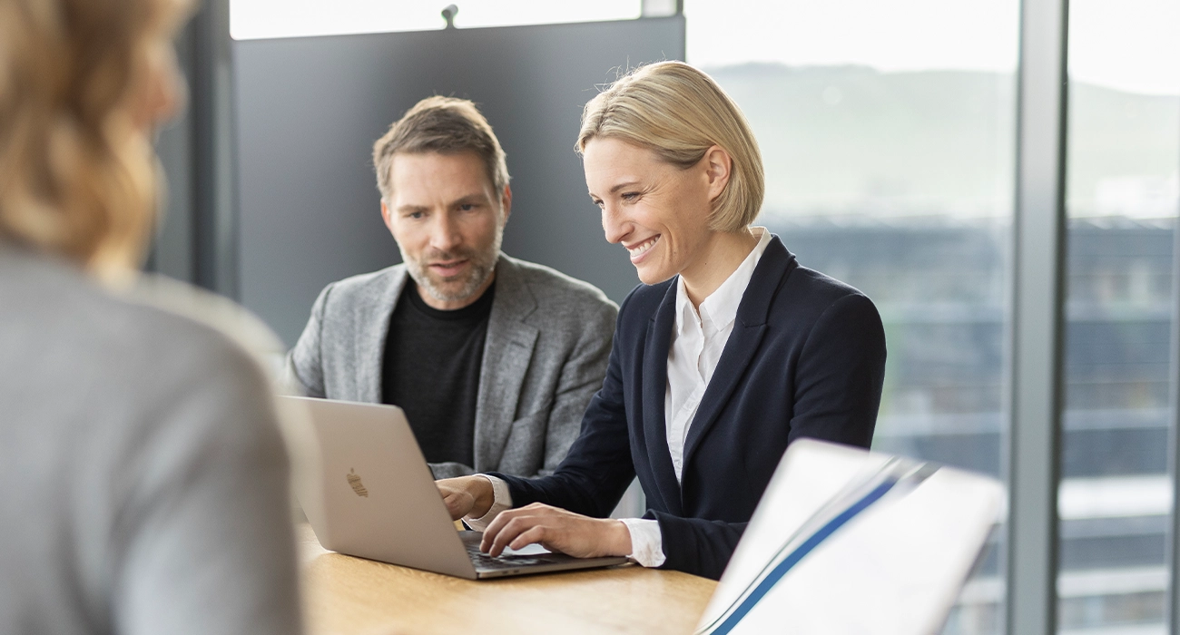 A man and a woman are working together on a laptop and smiling.