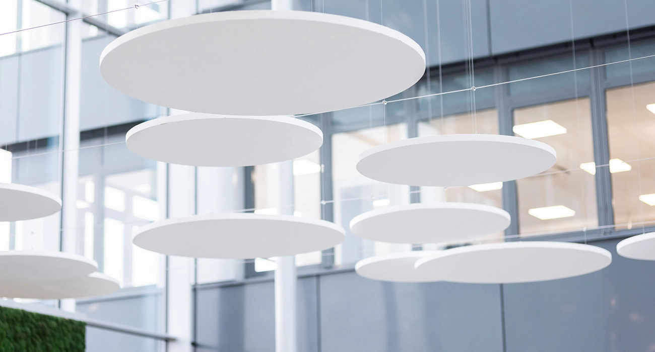 Several white, round ceiling panels hang in a bright room with high ceilings and an open-plan layout.