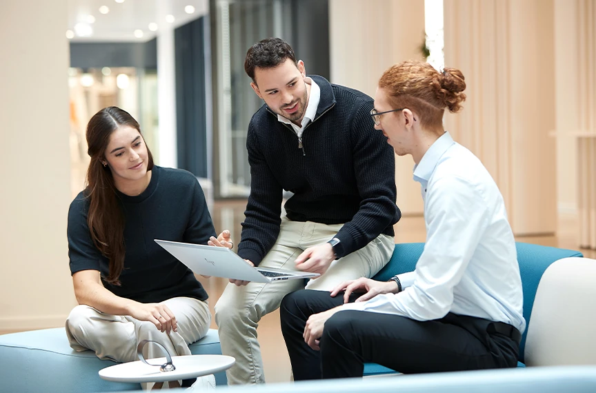 Two men and a woman are deep in conversation - the person in the middle is holding a laptop.