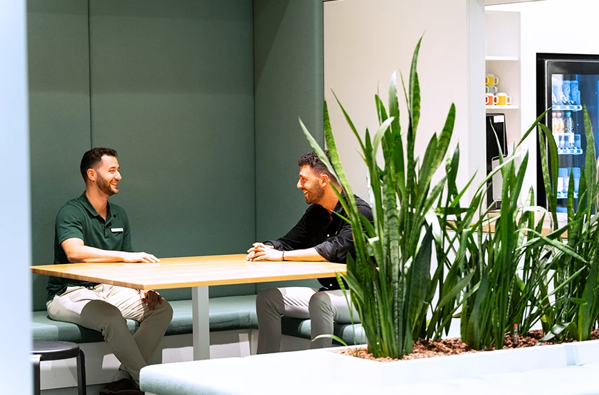 Two men are sitting at a table, laughing together and having a conversation.