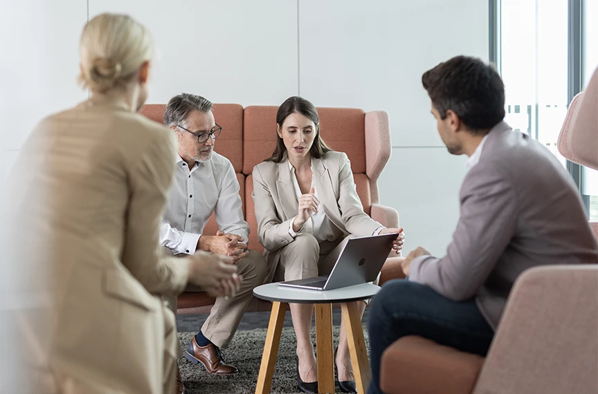 Two men and two women are sitting in a circle, whilst two of them are looking at a laptop together.