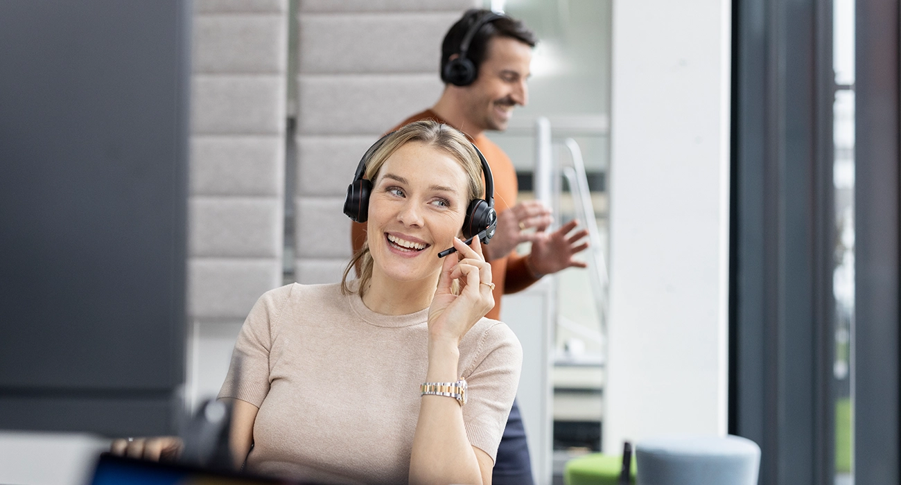 Zwei Bechtle-Mitarbeitende, im Vordergrund eine Frau mit Headset während eines Anrufs.