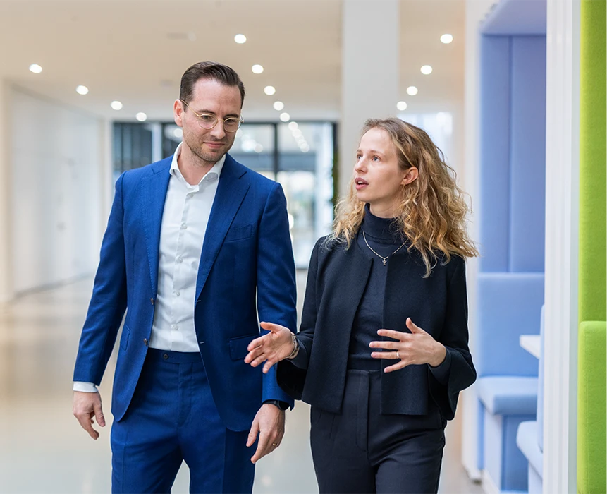 The image shows two individuals in a corporate environment engaged in what seems to be a conversation or discussion.