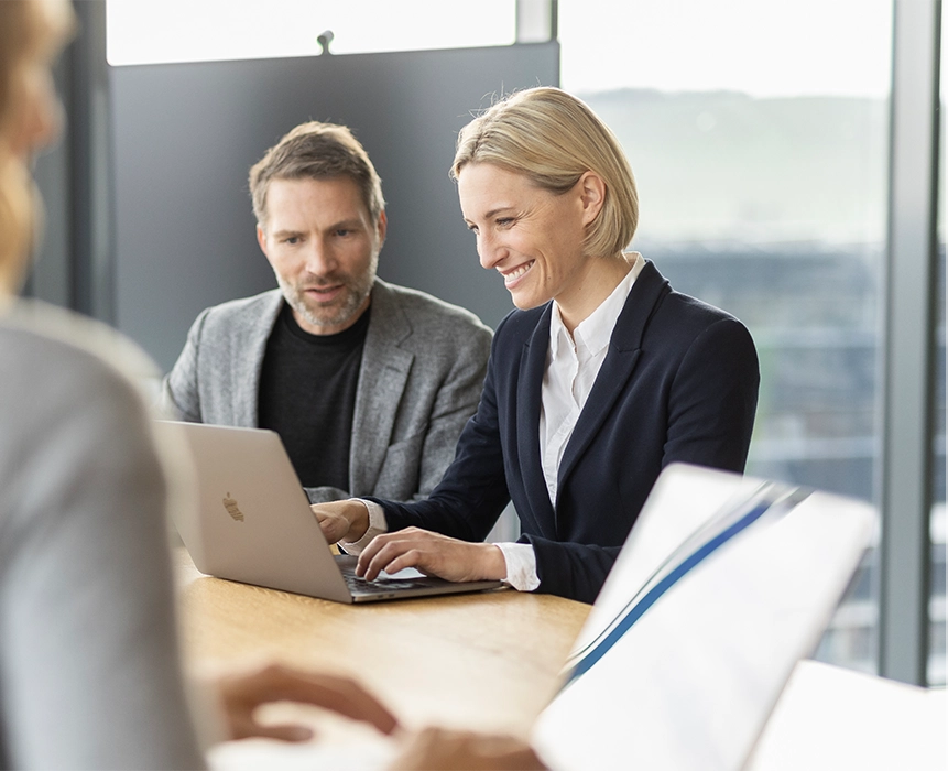 Ein Mann und eine Frau arbeiten gemeinsam an einem Laptop und lächeln.